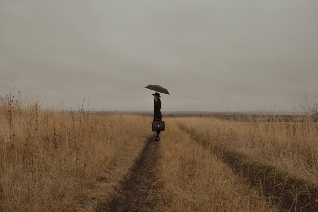 mujer vestida de negro con una maleta sola en medio del campo