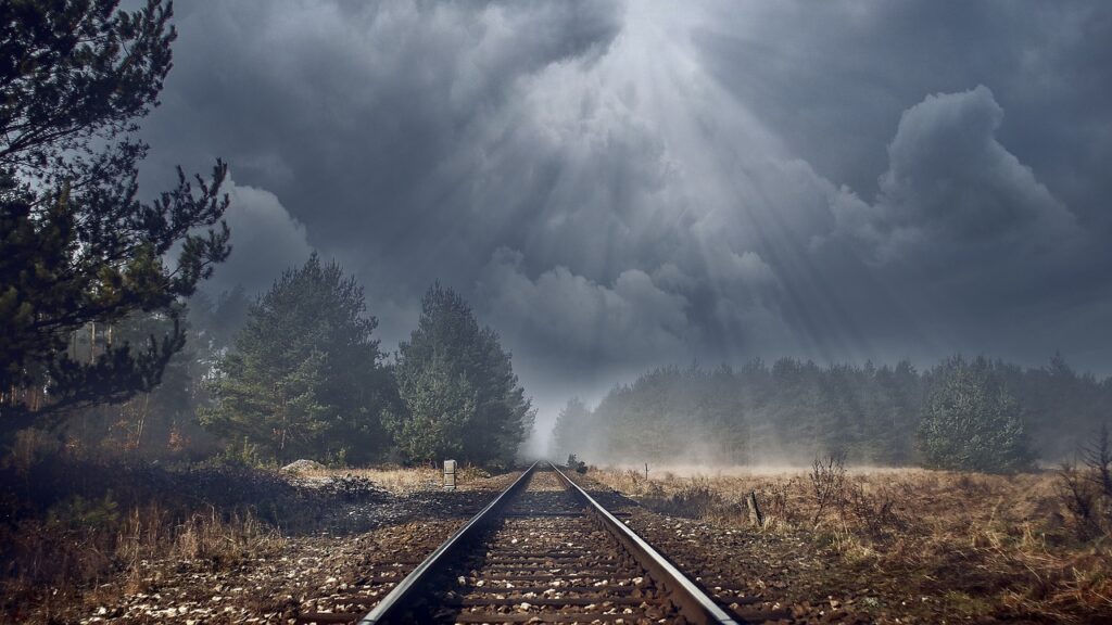 vía del tren que transcurre entre nubes y se dirige a un lugar soleado